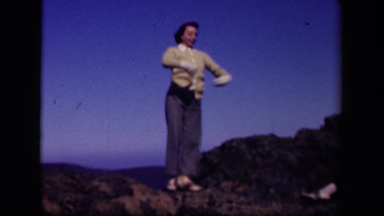 At Skyline Drive, Virginia, a woman in 1940s-style clothing stands on rocky ground with one arm extended beneath a deep blue sky.