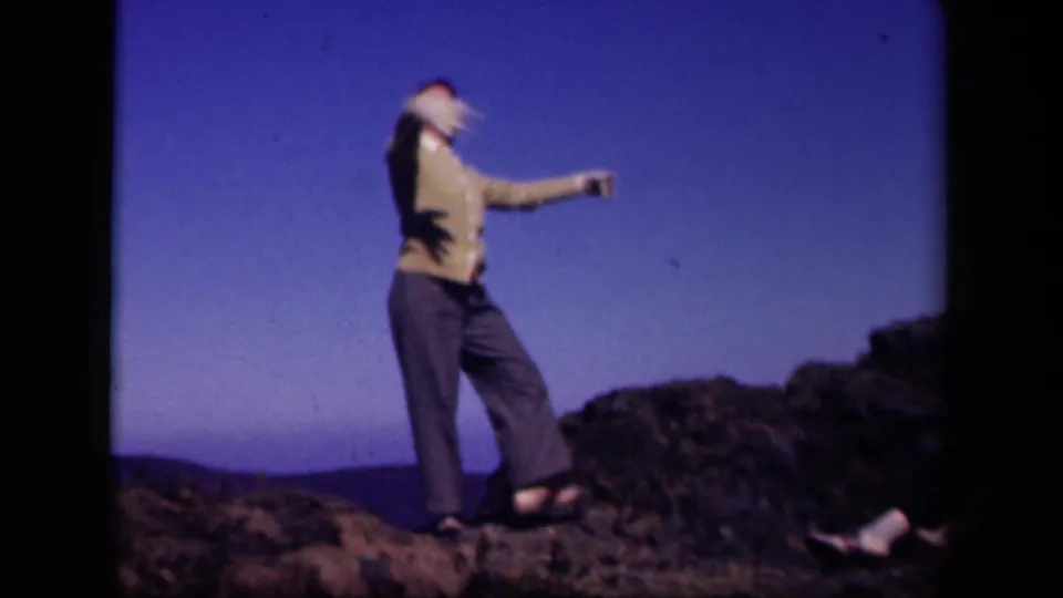 In a soft 8mm frame, the woman leans back in a lively dance pose on rocky ground at the Virginia travel stop.