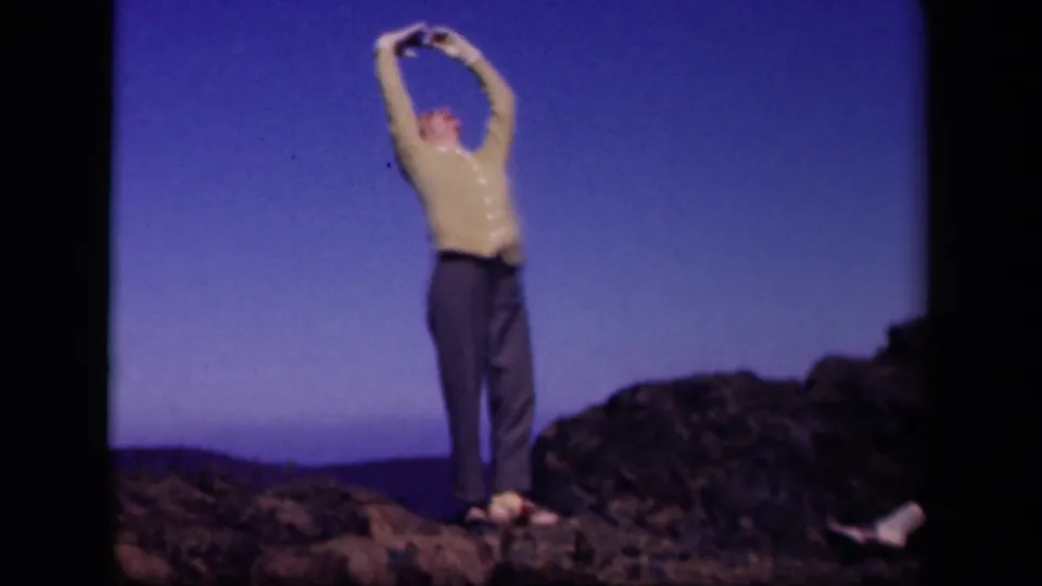 The woman finishes with arms raised high on the rocky Skyline Drive overlook, framed by blue sky and dark rocks.