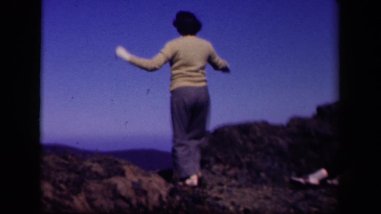 Woman seen from behind with arms raised while standing on rocks.