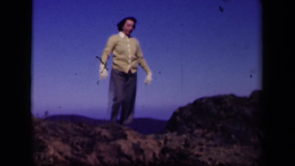 A woman in a cardigan, trousers, and white gloves faces the camera while dancing on rocks at Skyline Drive, Virginia.