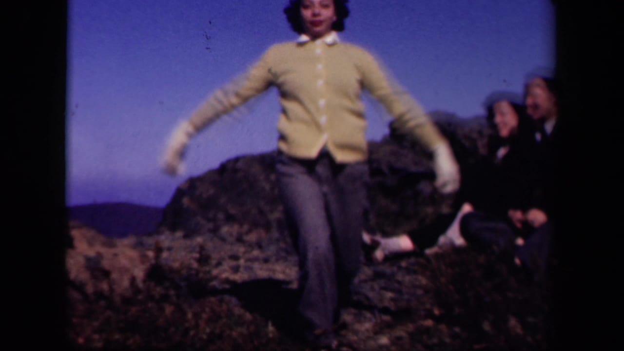 Young woman in a yellow cardigan poses on a rocky overlook with seated companions behind her.