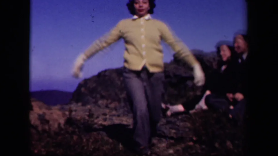 At Skyline Drive in 1943, a young woman in a yellow cardigan moves toward the camera on rocks while companions sit behind her.
