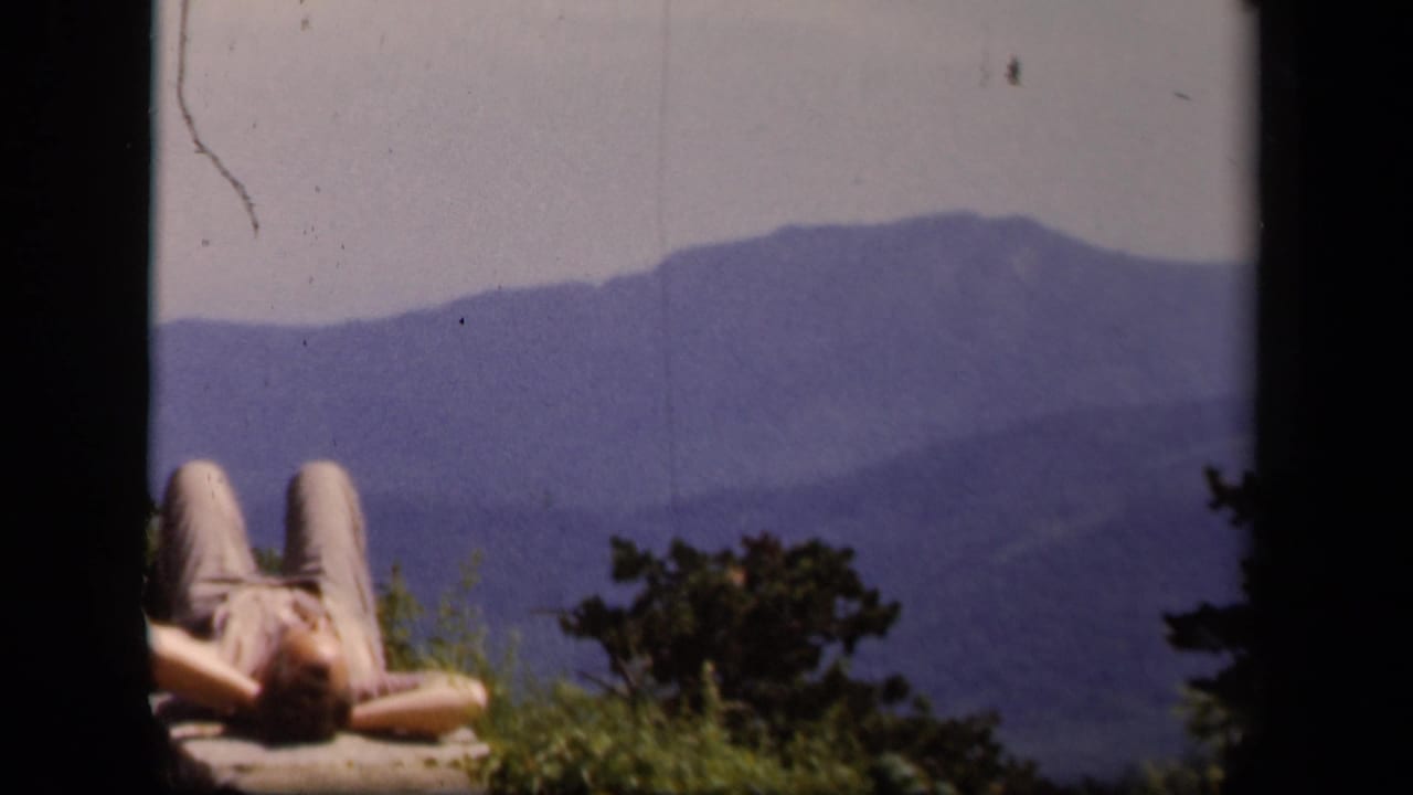 At Skyline Drive in Virginia, a person reclines on a stone overlook wall with blue mountain ridges in the distance.