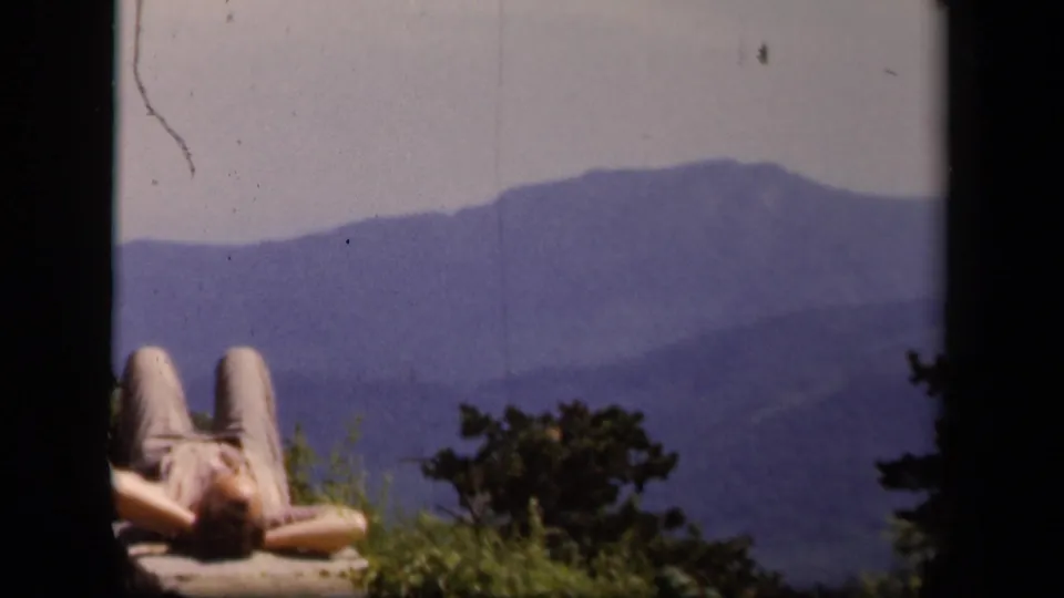 At Skyline Drive in Virginia, a person reclines on a stone overlook wall with blue mountain ridges in the distance.