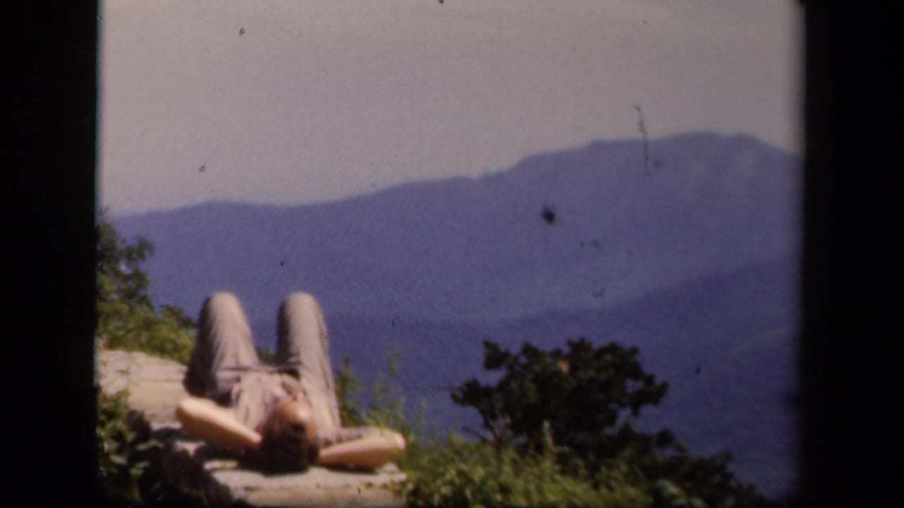 A 1943 Skyline Drive home-movie frame shows a person sunning on a stone wall above distant mountain ridges.