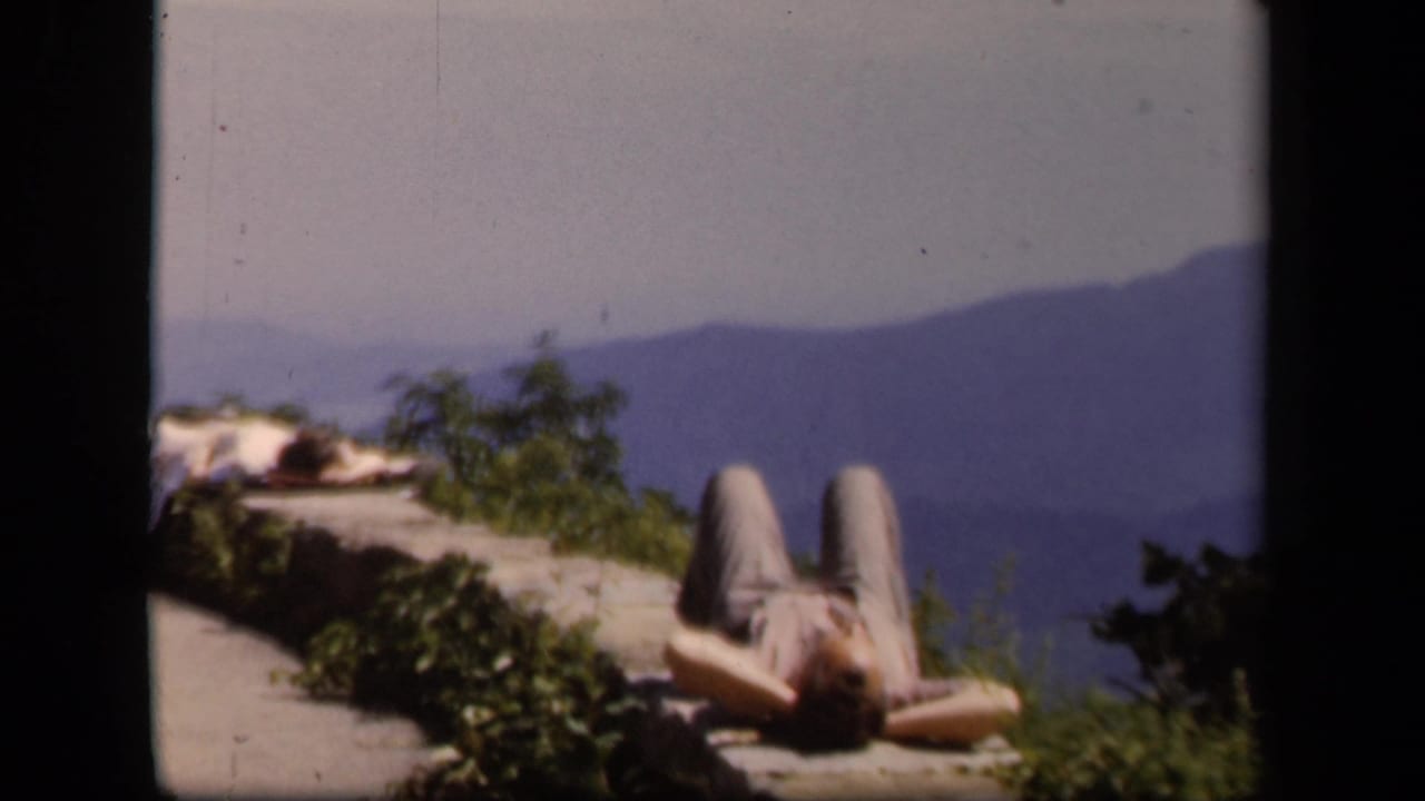 1943 Skyline Drive home-movie frame showing a person resting on a stone overlook above distant Virginia mountain ridges.