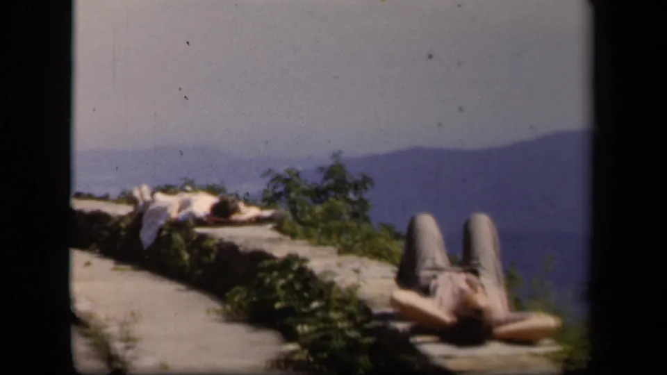 Color 8mm frame from Skyline Drive showing a relaxed visitor on a stone ledge overlooking Virginia mountains.