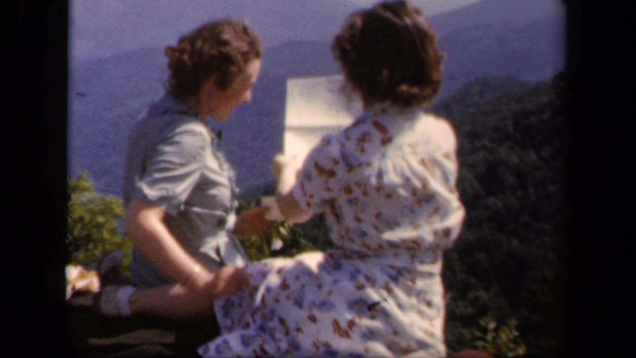 Two women at Skyline Drive, Virginia in 1943 sit near an overlook and look toward a paper map with hazy mountains behind them.