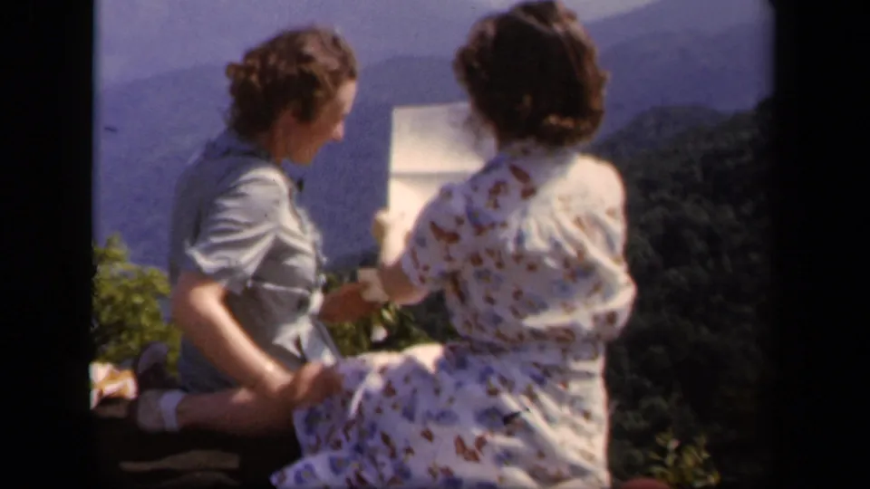 Two women at Skyline Drive, Virginia in 1943 sit near an overlook and look toward a paper map with hazy mountains behind them.