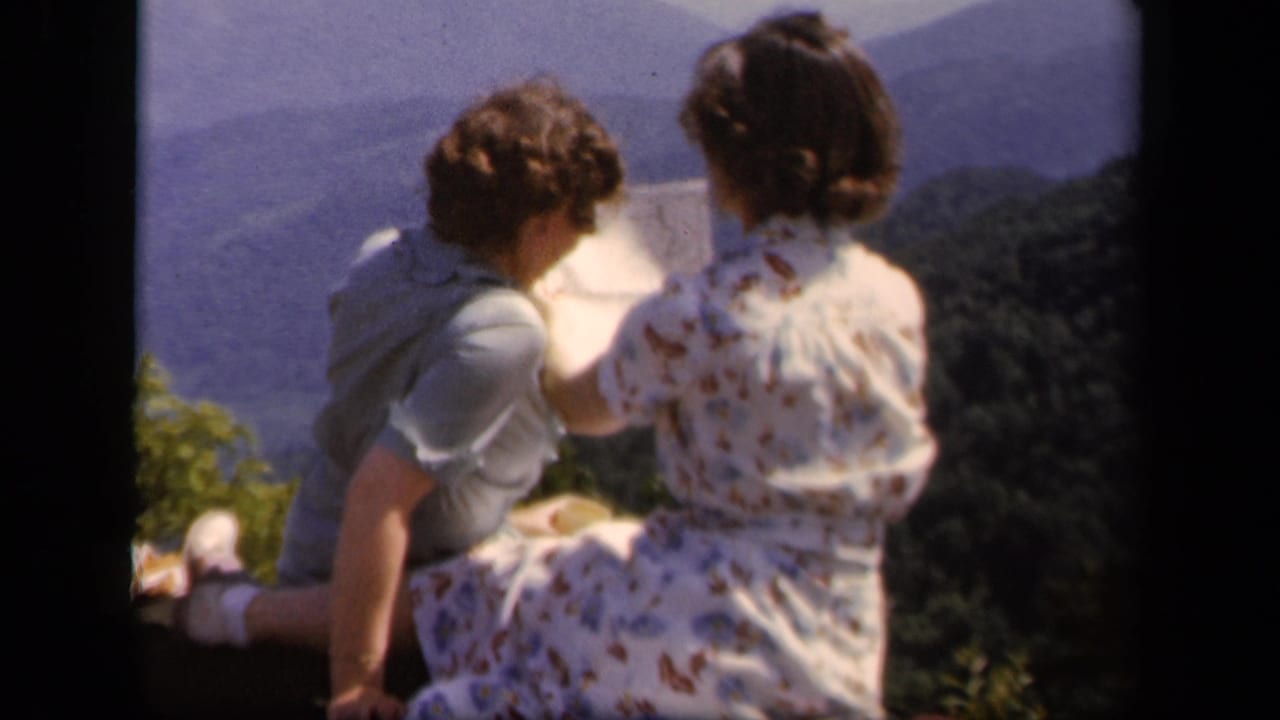 Two women sit side by side at an overlook while one points toward a paper map.