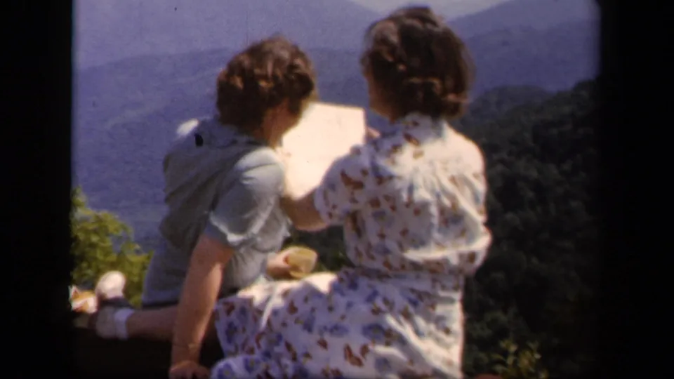 The women continue looking at a map from a Skyline Drive overlook, with hazy Blue Ridge mountains filling the background.