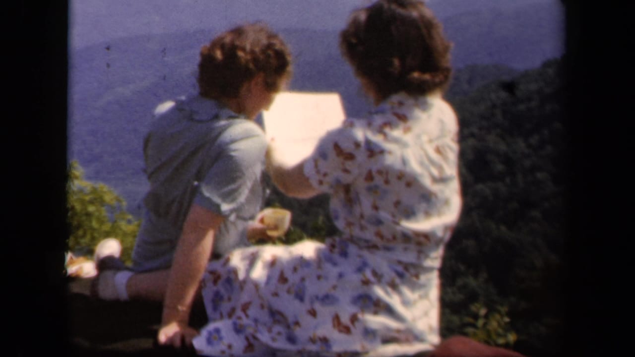 At Skyline Drive in 1943, two women sit near an overlook with blue mountain ridges behind them as one holds a pale paper or booklet.