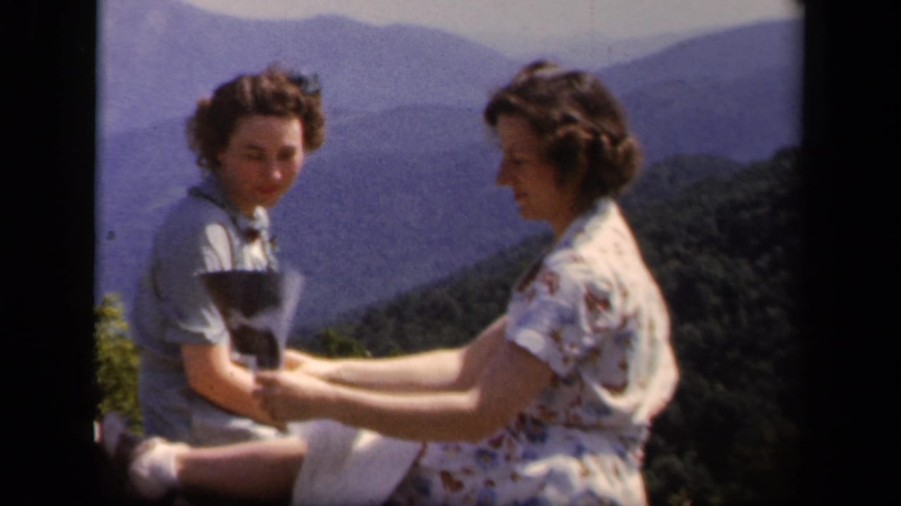 Two women sit at a mountain overlook while one holds a folded map.