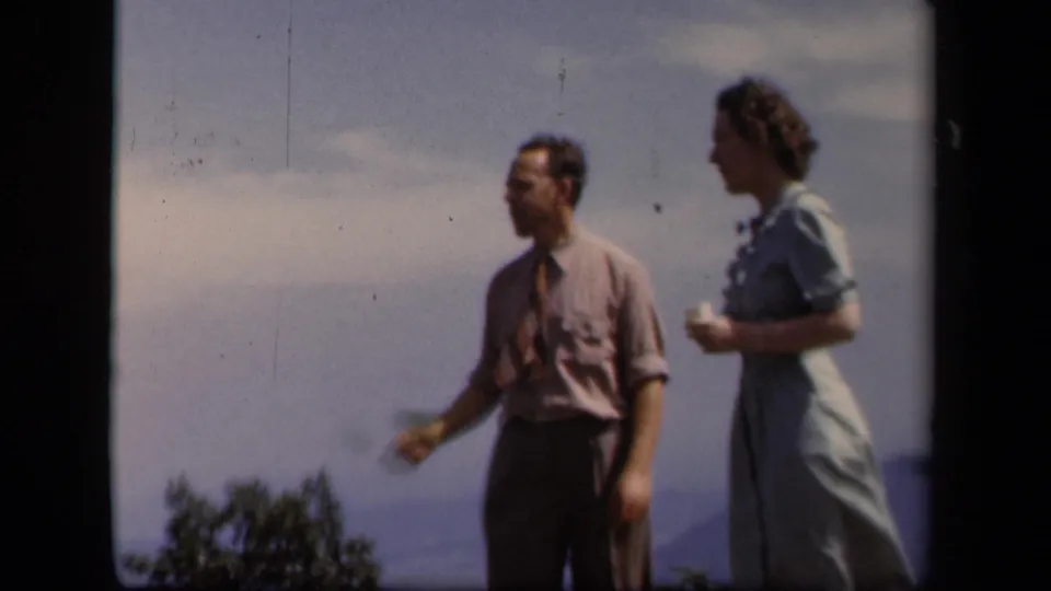 A man and woman stand at a Skyline Drive vista, with the man holding a small leaf or object and distant ridges behind them.