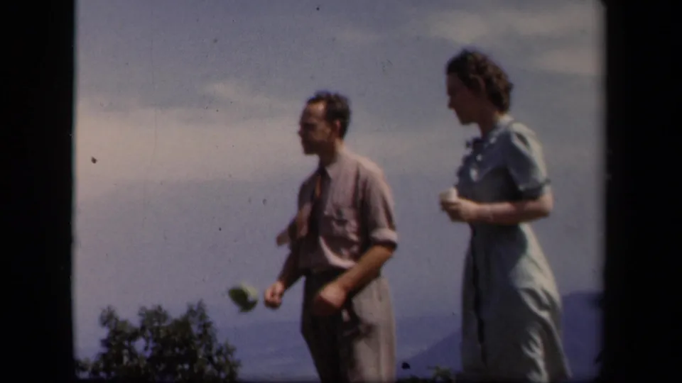 A man and woman stand side by side at the Skyline Drive overlook, one holding a small object and the other holding a cup.