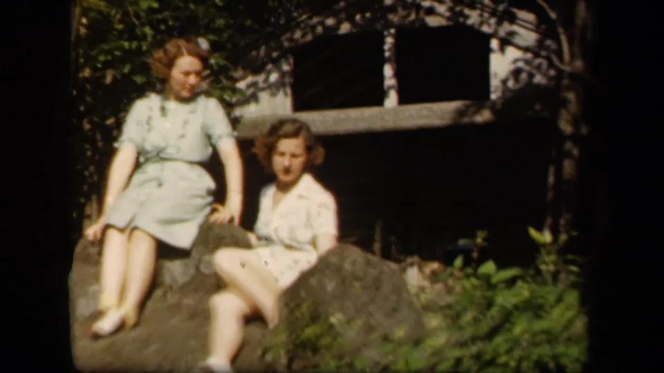 Two women in 1940s dresses sit on rocks at Skyline Drive, Virginia, as one looks more directly toward the camera.