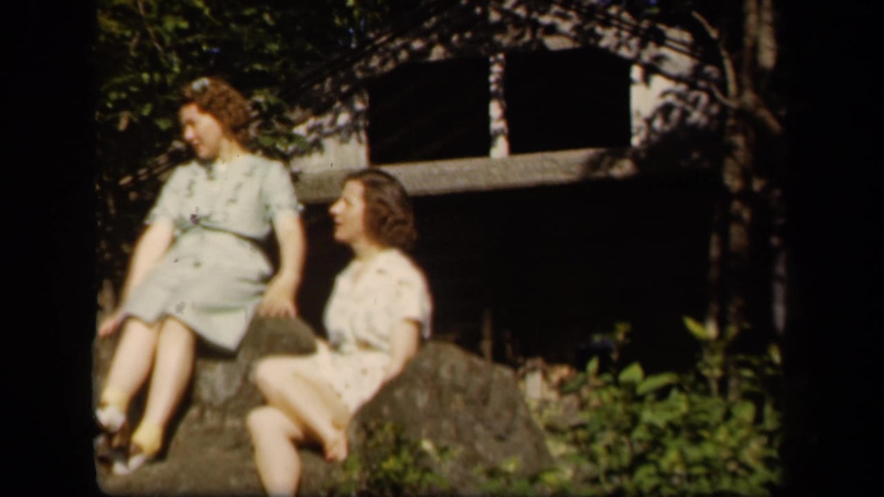 Two women sit close together on rocks, turned toward one another outdoors.