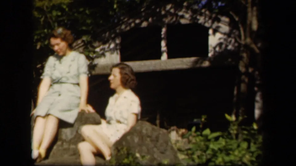 Two adult women wearing period dresses sit among rocks and greenery in 1943 Skyline Drive home-movie footage.