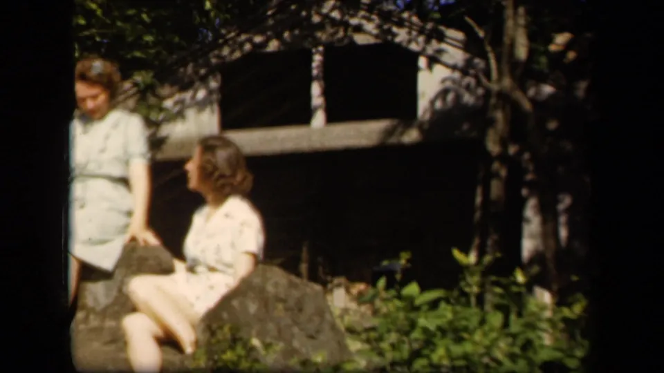 In the final frame, two adult women sit on rocks at the supplied Skyline Drive setting, with foliage and a shaded structure behind them.