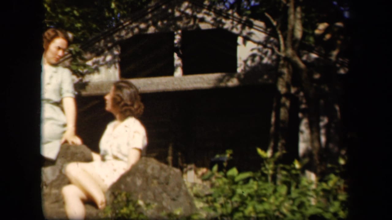 Two young women in light dresses appear outdoors at Skyline Drive, Virginia, in 1943 home-movie footage, seated and standing near rocks and trees.