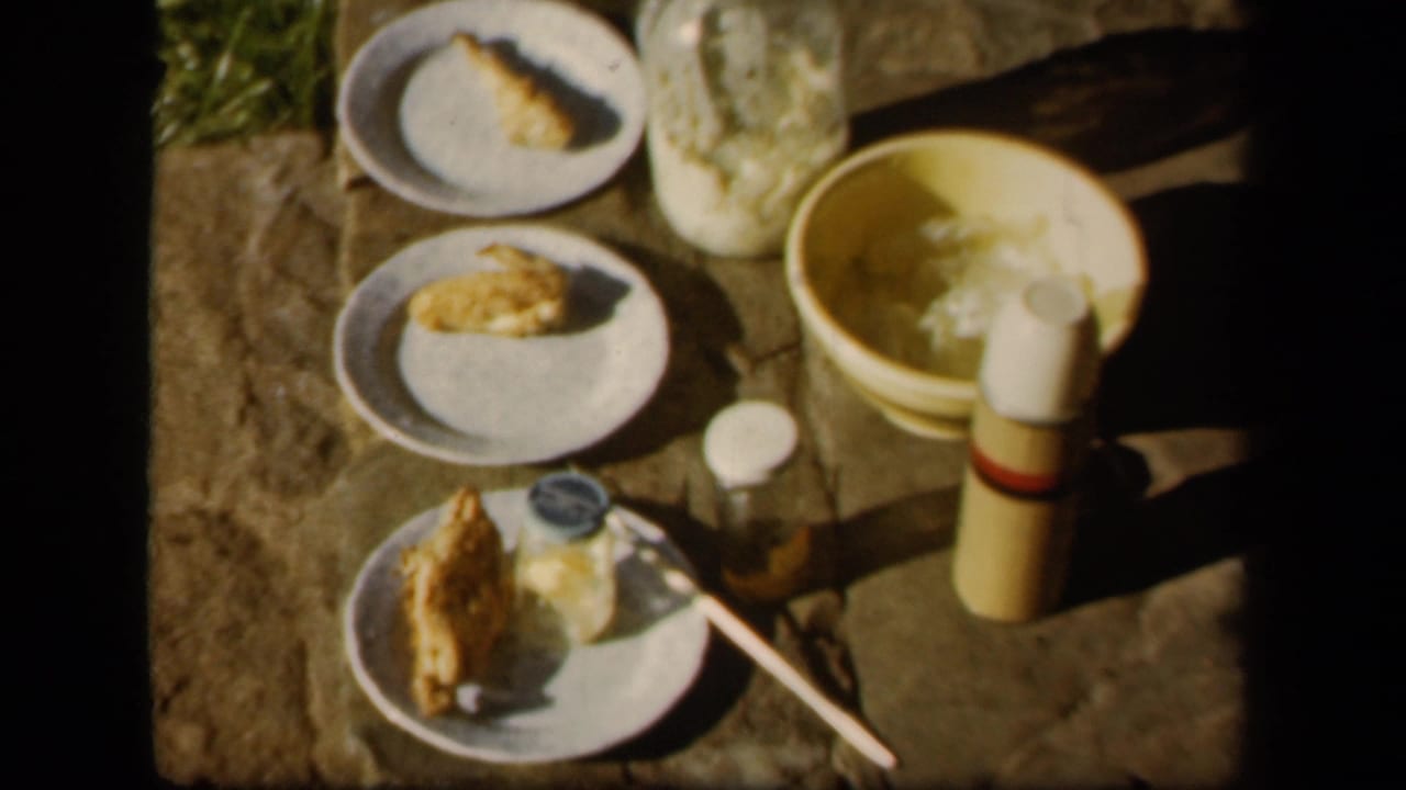 Plates of food, jars, a thermos, and a bowl arranged on an outdoor surface.
