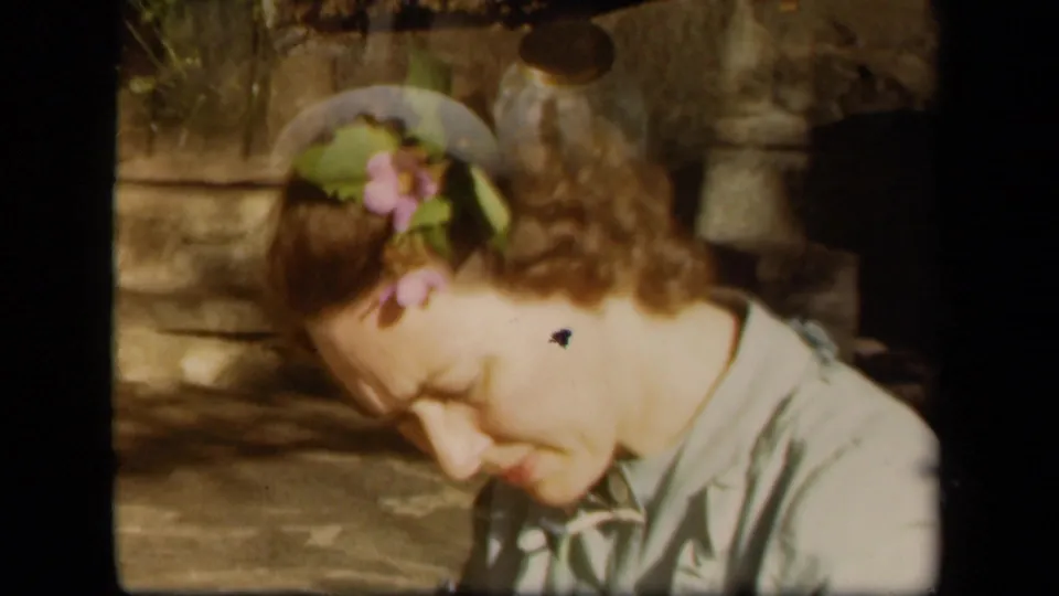 Adult woman with flowers in her hair looks down in concentration during 1943 Skyline Drive home-movie footage.