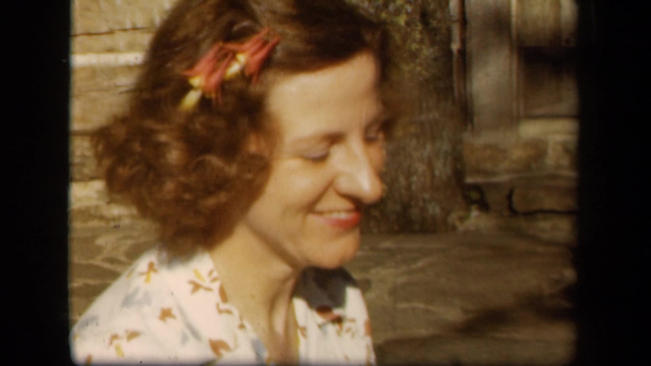 Woman with curled hair smiles beside a tree and rustic background.