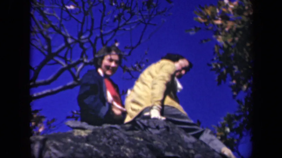 At Skyline Drive in 1943, two women on a rocky ledge look toward the camera, one in a dark coat and one in a yellow jacket.