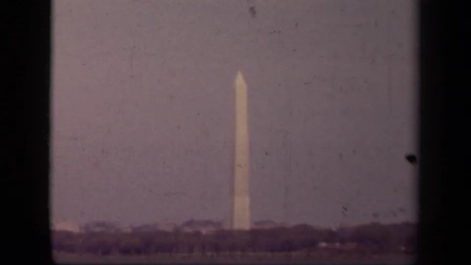 The Washington Monument appears centered against a pale sky, with a dark tree line and visible 8mm edge marks.