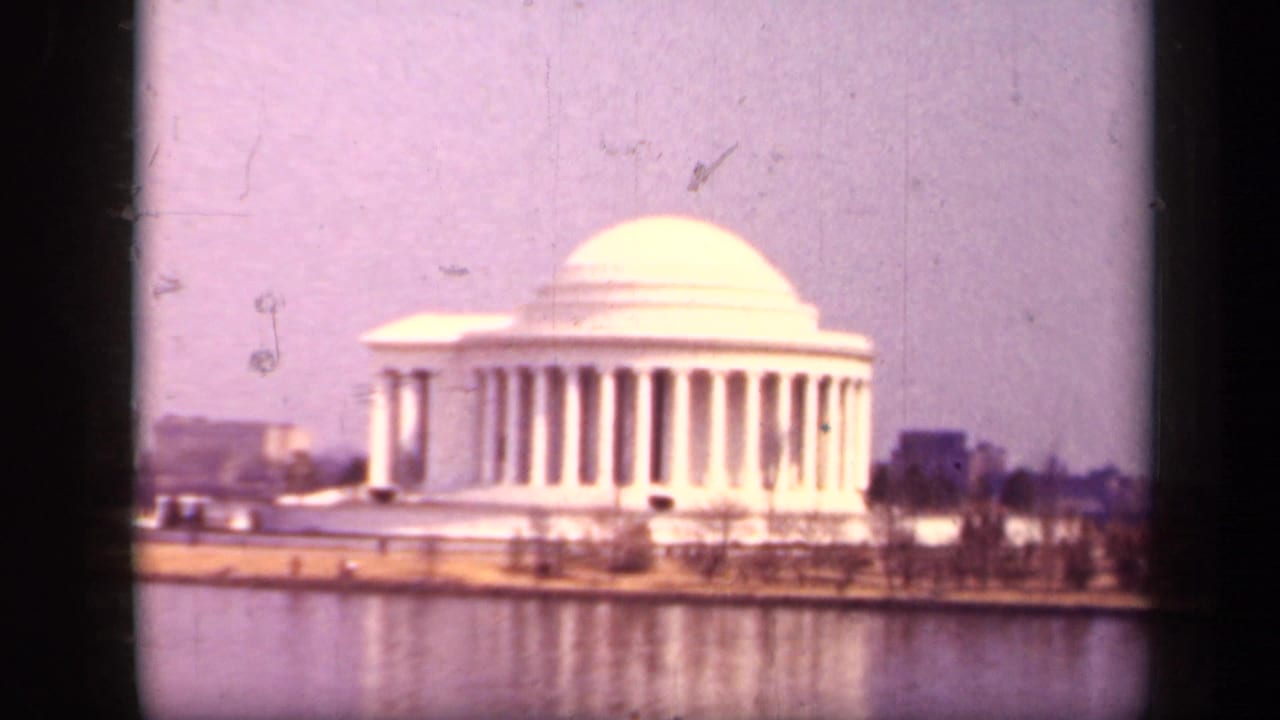 1943 8mm view of the Jefferson Memorial in Washington, D.C., seen across the Tidal Basin with dome, columns, shoreline, and reflection.
