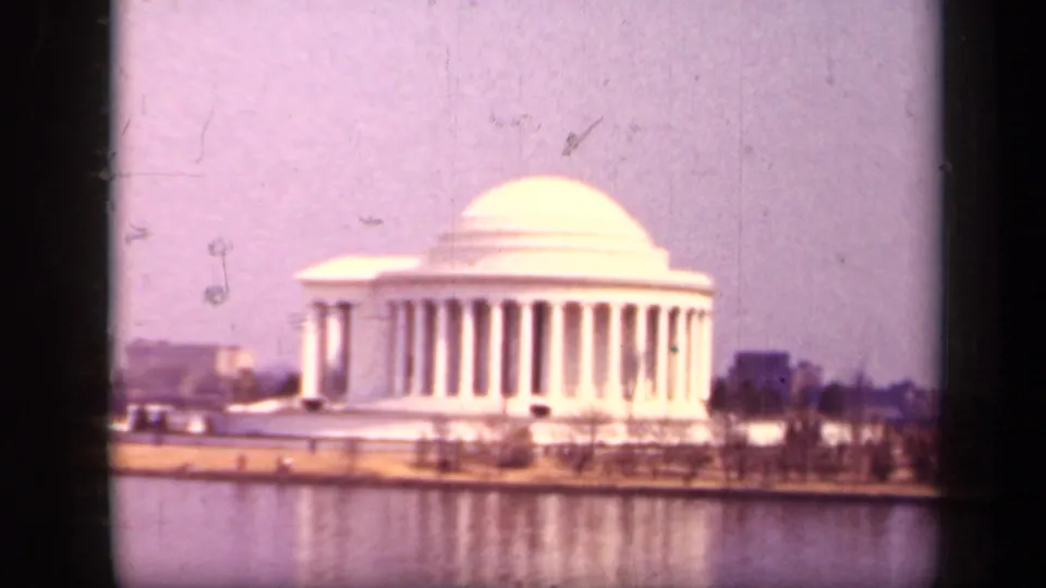 1943 8mm view of the Jefferson Memorial in Washington, D.C., seen across the Tidal Basin with dome, columns, shoreline, and reflection.