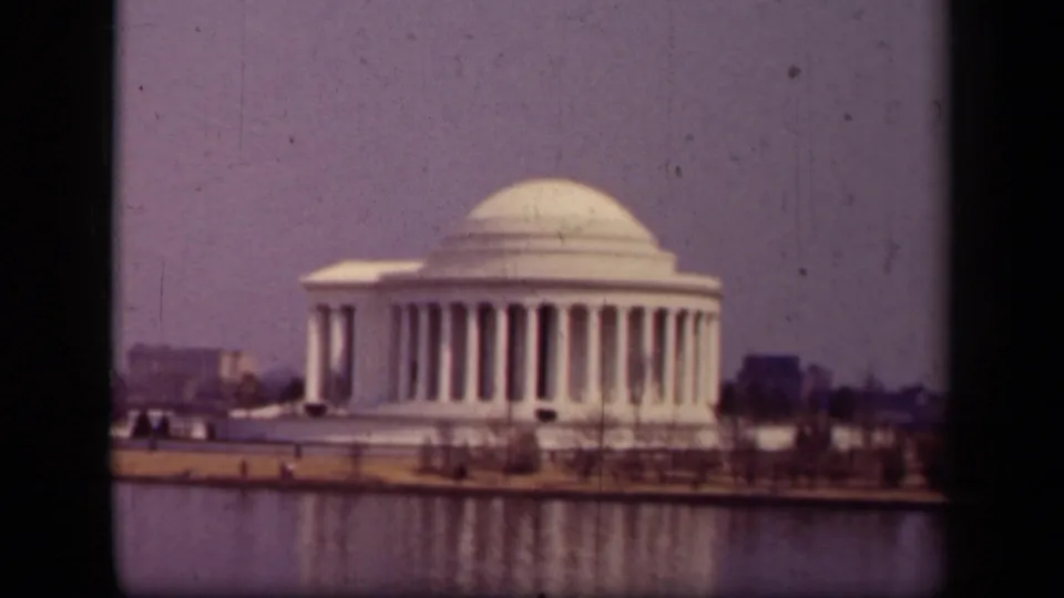 1943 Washington, D.C. home-movie frame showing the Jefferson Memorial across the Tidal Basin, with columns, dome, shoreline, and muted sky.