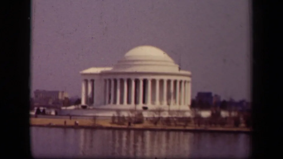 1943 home-movie view of the Jefferson Memorial beside the Tidal Basin, with the white dome, columns, reflection, trees, and distant buildings visible.