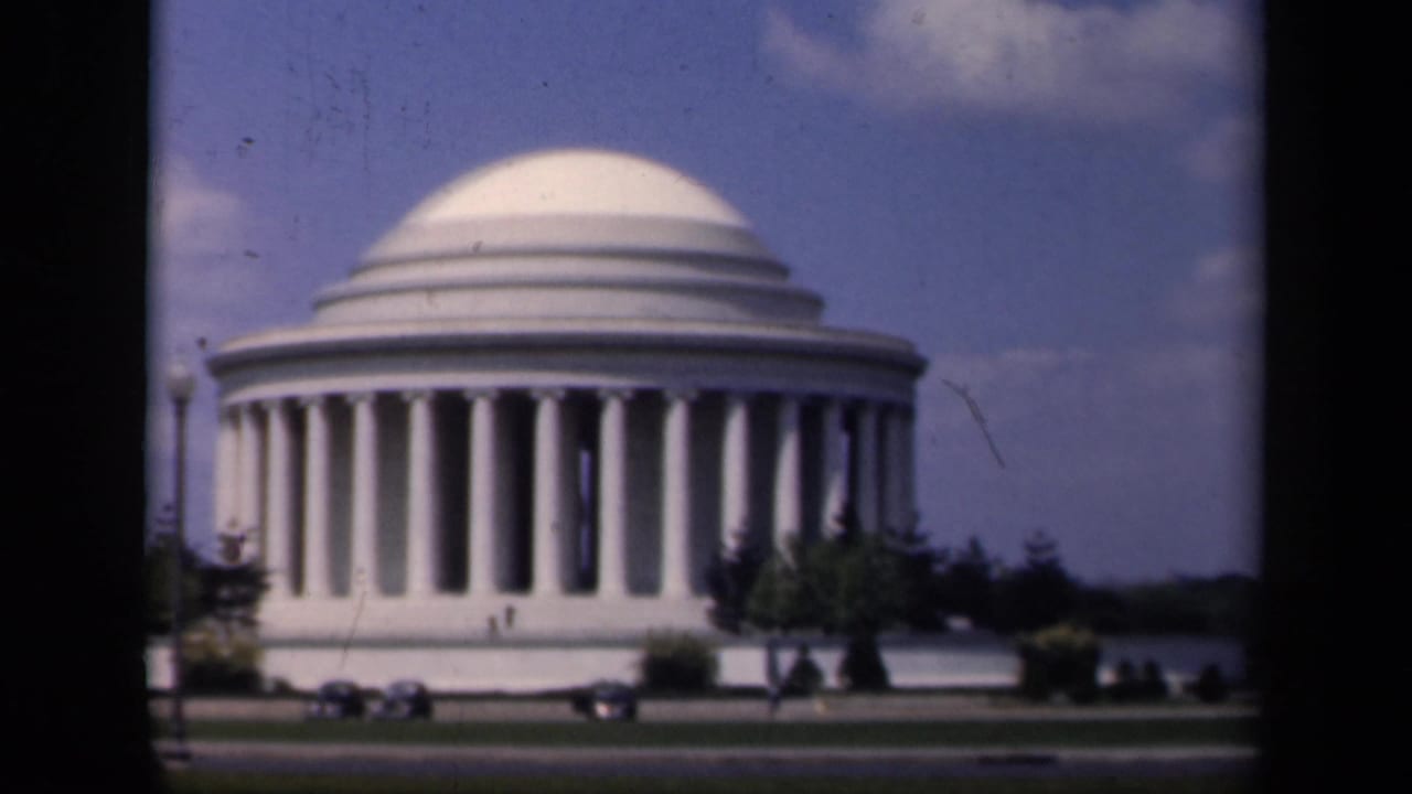 Jefferson Memorial centered behind a road with small cars and trees visible.