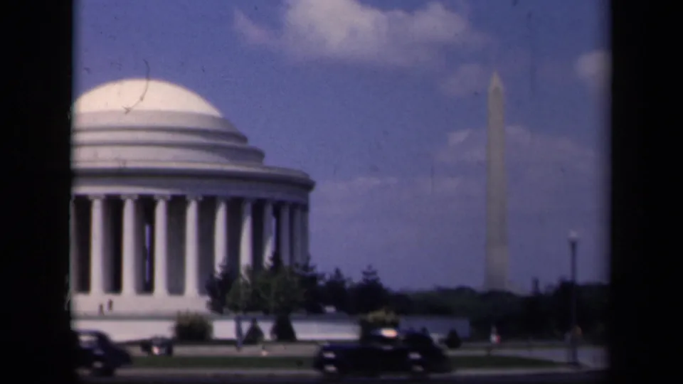 Soft 8mm view of the Jefferson Memorial and Washington Monument in Washington, D.C., with cars moving across the lower frame.