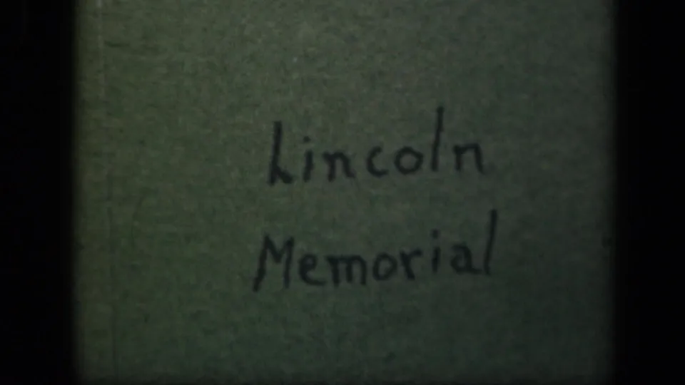 Close view of a handwritten Lincoln Memorial title card on aged paper, scanned from 8mm footage with visible grain and edge shadowing.