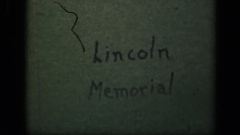 Aged 8mm title frame reading Lincoln Memorial, with a dark scratch-like mark, greenish paper tone, and heavy film grain.