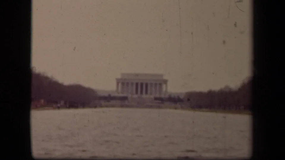 Washington, DC home-movie frame showing the Lincoln Memorial across rippled water with bare trees at the sides.