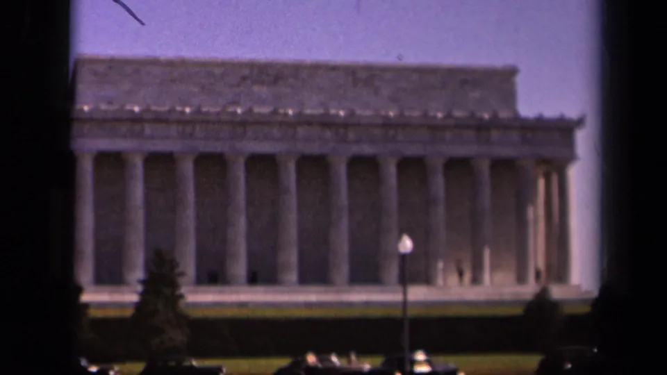 1943 8mm frame of the Lincoln Memorial from a visitor viewpoint, with columns, lawn, parked cars, and small distant visitors.