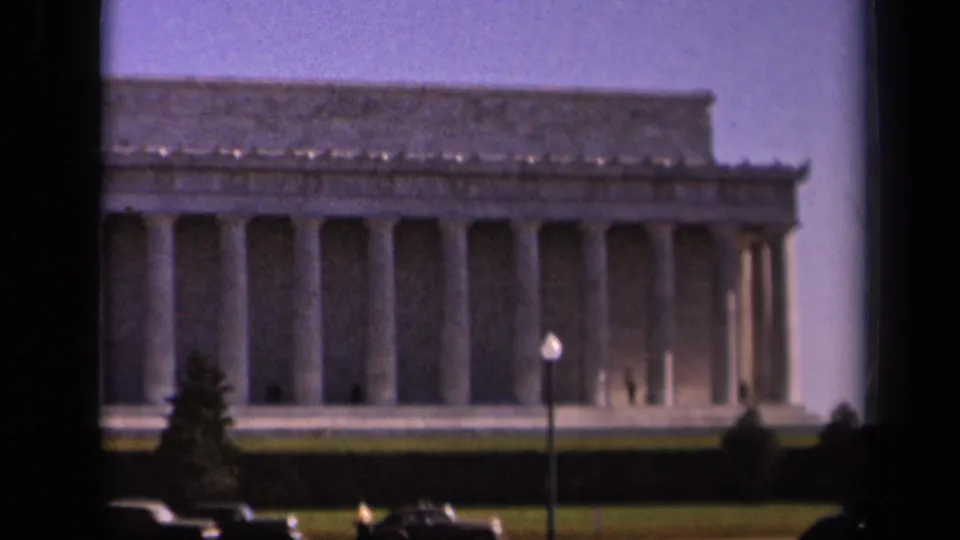 Soft 1943 home-movie view of the Lincoln Memorial in Washington, DC, with foreground cars, trees, lawn, and distant visitors.