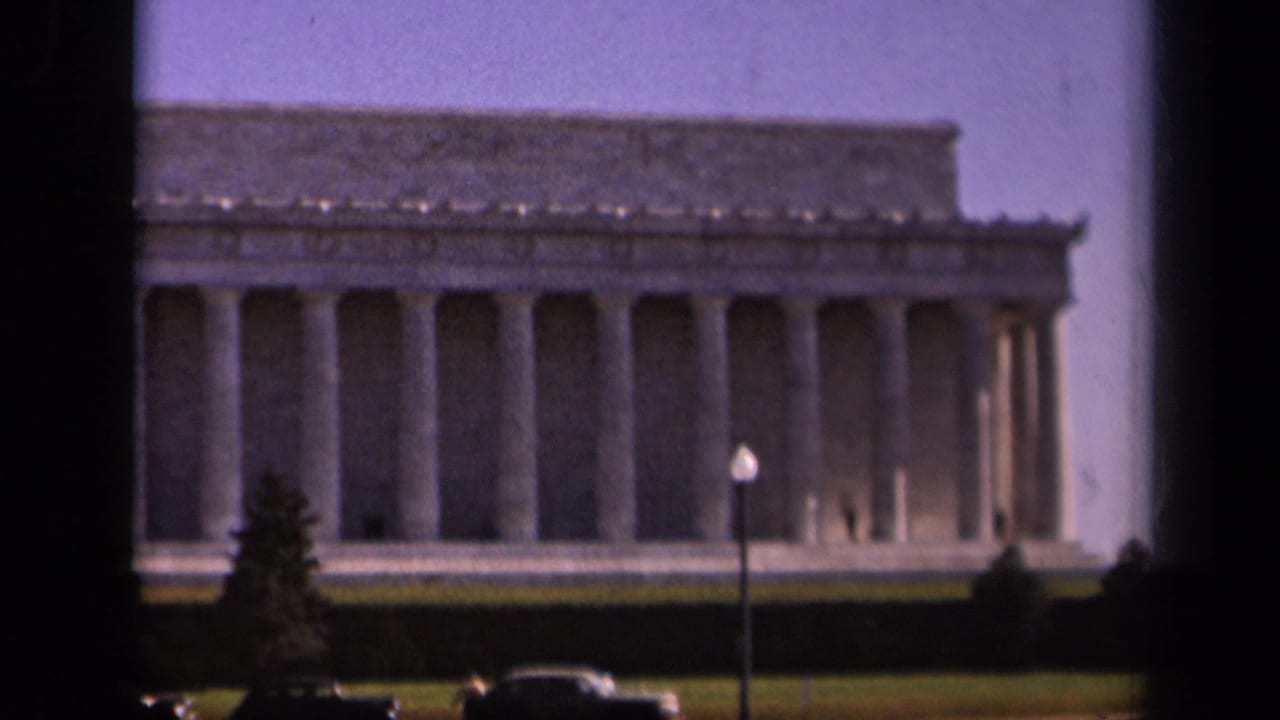 Lincoln Memorial seen across a lawn with columns, cars, and a lamppost in front.