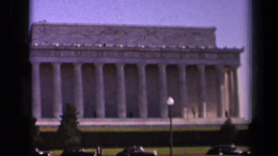 Soft 8mm frame of the Lincoln Memorial in Washington DC, showing columns, roofline, lawn, lamppost, and cars.