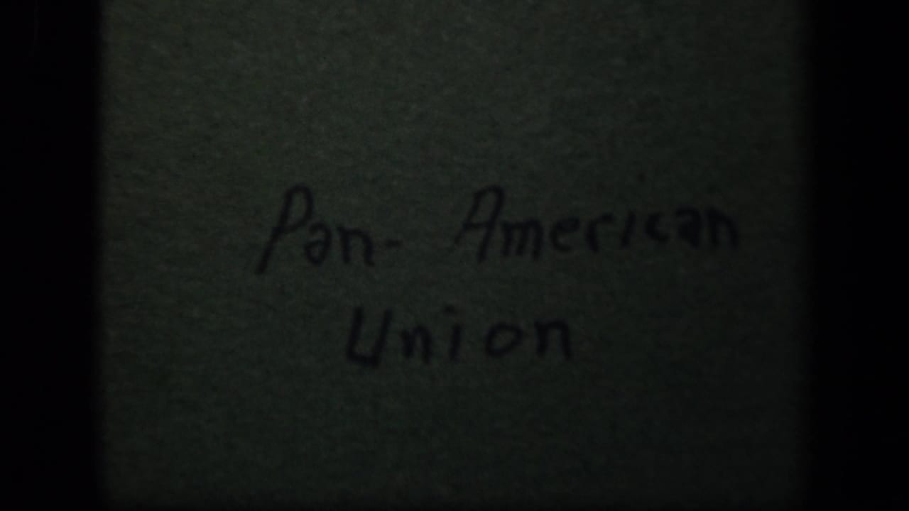 1943 8mm frame showing a handwritten Pan-American Union title card on a green textured surface, bordered by dark film shadows.