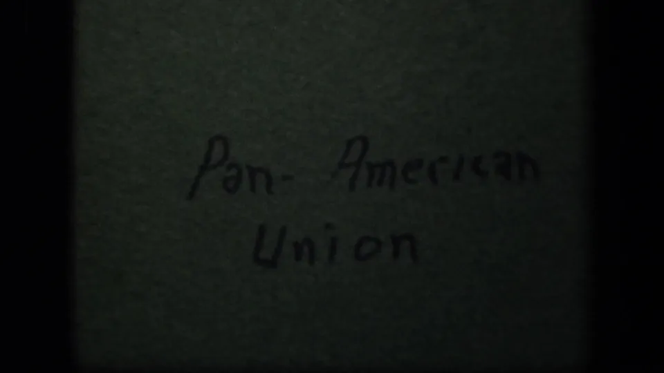 1943 8mm frame showing a handwritten Pan-American Union title card on a green textured surface, bordered by dark film shadows.