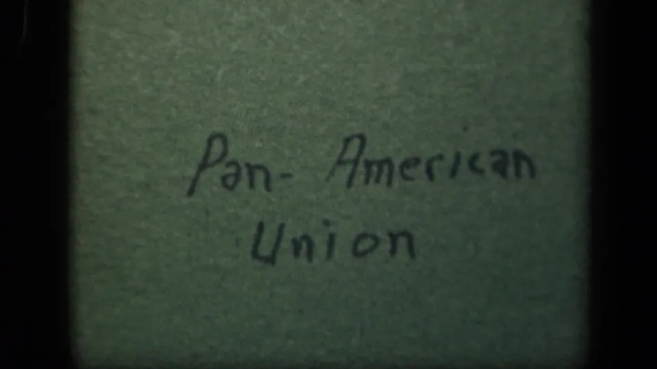 A brighter 8mm view of the handwritten Pan-American Union title card, with green surface texture and dark vertical frame edges visible.