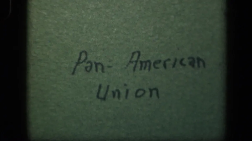 Close 8mm frame of the Pan-American Union handwritten title card on a green background, still partially shadowed by the film edge.