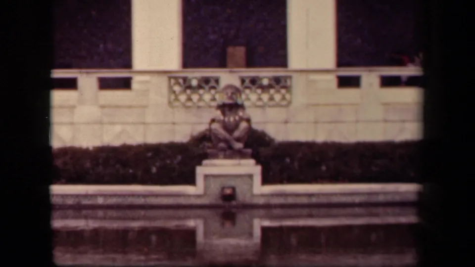 Final 1943 Washington, DC frame showing the costumed person seated near water, with a formal balustrade and pale columns in the background.