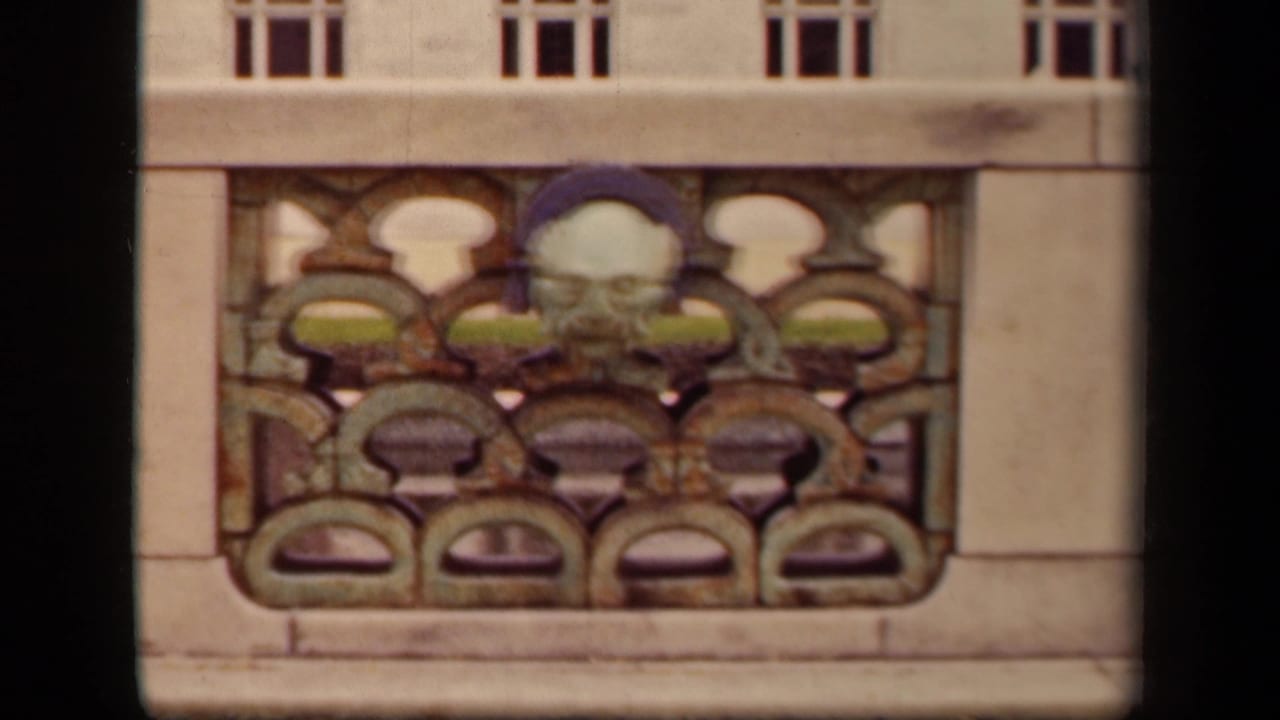 Ornate balcony railing with patterned metalwork and a sculpted mask-like face.