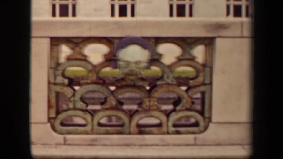 Close view of Washington DC architectural ornament with pale masonry, small windows, and a sculpted face in metalwork.